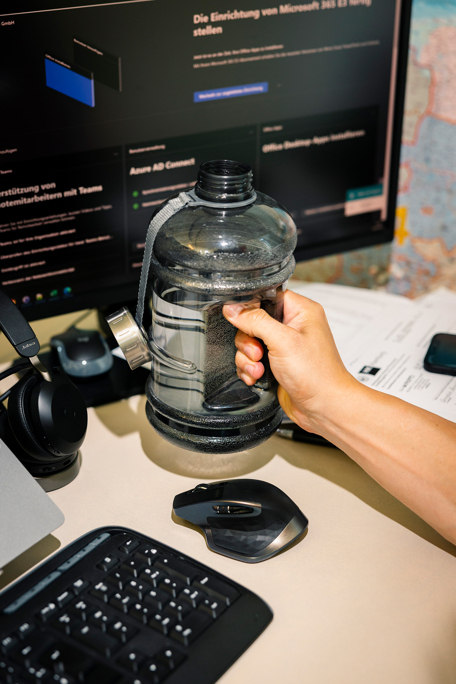 Eine Hand greift eine Wasserflasche auf einem Computerarbeitsplatz.